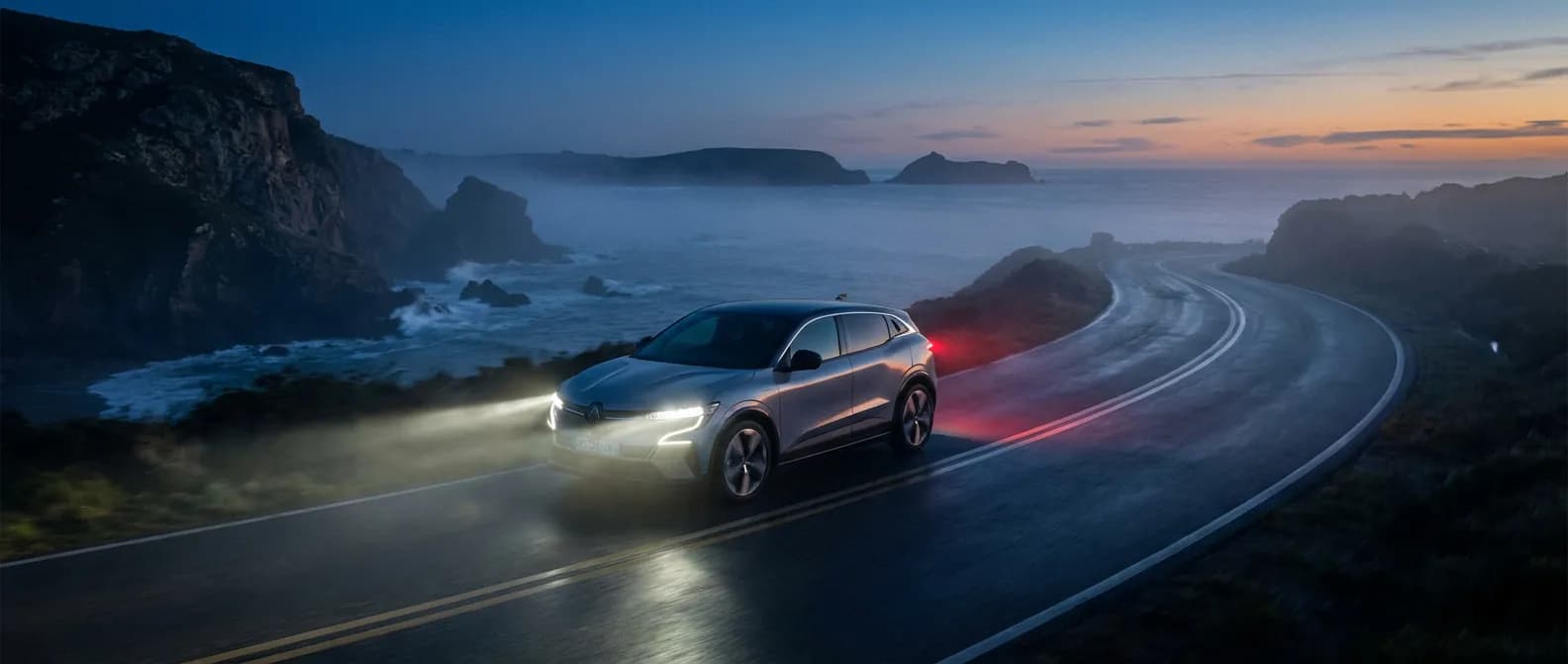 Vue cinématique d'un véhicule Renault E-Tech sur une route côtière soulignant la technologie de sa transmission