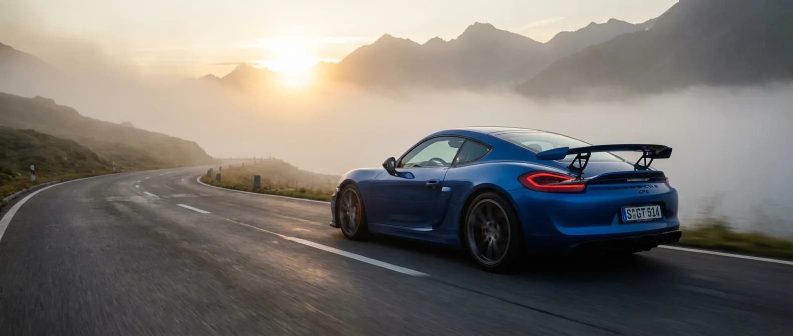 Porsche 981 GT4 bleue sur une route de montagne sinueuse au lever du soleil