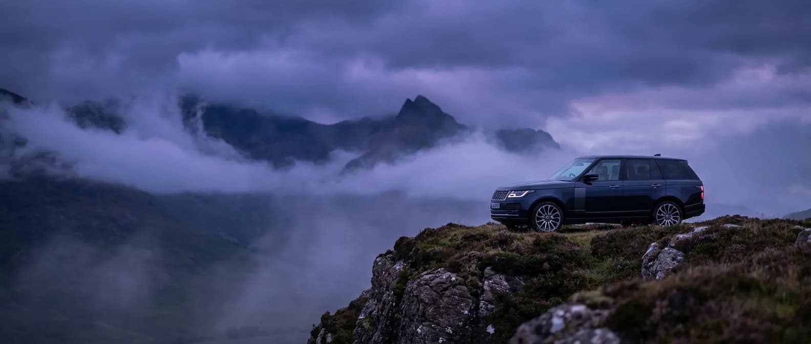 SUV de luxe Range Rover en haut d'une falaise brumeuse dans les Highlands, style éditorial haut de gamme.