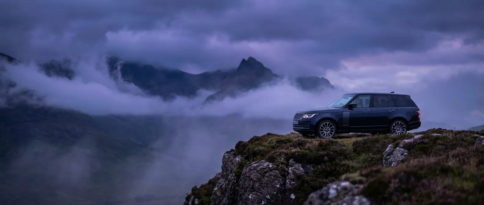 SUV de luxe Range Rover en haut d'une falaise brumeuse dans les Highlands, style éditorial haut de gamme.