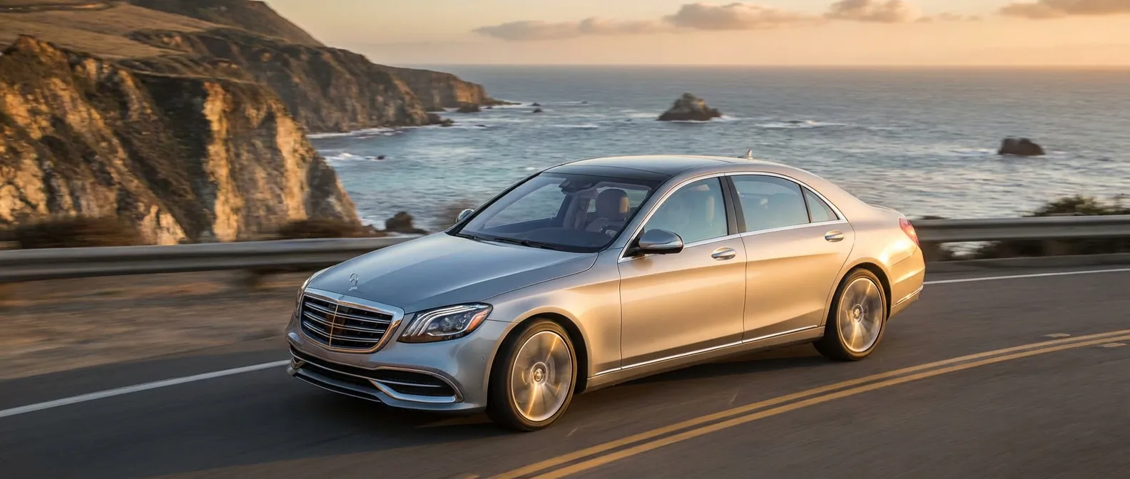 Une Mercedes-Benz de luxe circulant sur une route panoramique au soleil couchant.